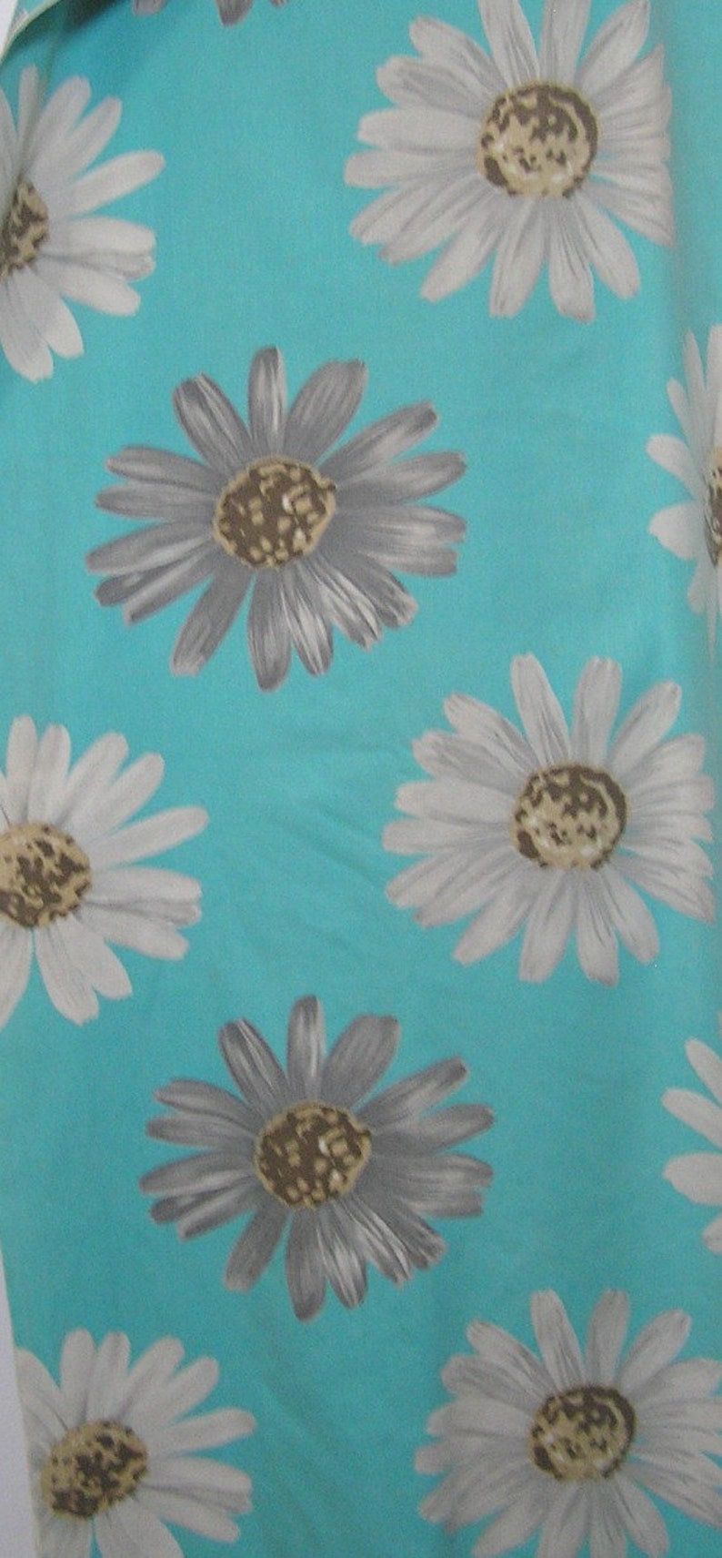 May include: A turquoise fabric with a repeating pattern of white and gray daisies. The daisies have brown centers.