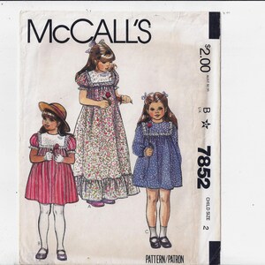 May include: McCall's sewing pattern for children's dresses, pattern number 7852, child size 2. The pattern includes three different dress styles: a floral print dress with a ruffled hem, a blue dress with a ruffled neckline, and a red and white striped dress with a Peter Pan collar.