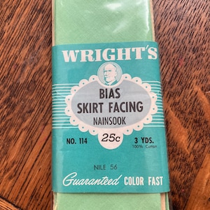 Può includere: Un pacchetto di tessuto verde per orlo di gonna a sbieco della marca Wright's. Il pacchetto è etichettato con il nome del prodotto, il numero 114, il prezzo 25c e 3 iarde di cotone 100%. L'etichetta riporta anche "Nile 56" e "Colore garantito",