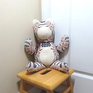 May include: A large, plush, white, pink, and blue tiger stuffed animal sits on a wooden stool. The tiger has a white face with a black nose and black eyes.