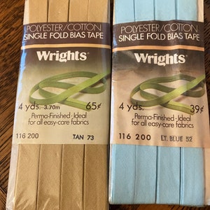 May include: Two packages of Wrights single fold bias tape. The package on the left is tan and the package on the right is light blue. Both packages are 4 yards long and are made of polyester and cotton. The tan package is 65 cents and the light blue package is 39 cents.
