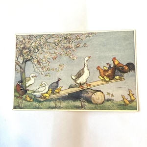 May include: A rectangular print featuring a whimsical illustration of a large white goose standing on a wooden seesaw balanced on a log. Various ducks, chickens, chicks, and a guinea fowl are gathered around the seesaw under a flowering tree.
