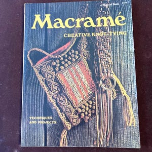 May include: A vintage book cover titled "Macrame" with the subtitle "Creative Knot Tying." The cover features a detailed macrame bag with red, white, and brown woven patterns. The words "Techniques and Projects" are also visible.