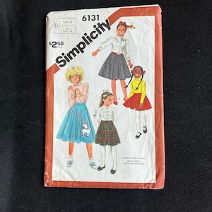 May include: Simplicity sewing pattern number 6131 for girls' skirts. The pattern includes instructions for three different skirt styles: a blue skirt with a poodle applique, a plaid skirt, and a black skirt. The pattern is for sizes 7-8-10.