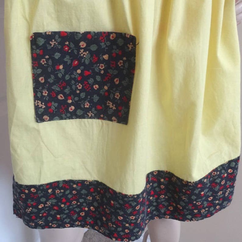 May include: A yellow cotton dress with a floral print pocket and a floral print trim around the bottom hem.