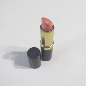 May include: A closed tube of lipstick with a gold band and a pink lipstick bullet. The tube is navy blue.
