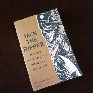 May include: A book titled "Jack the Ripper: First American Serial Killer" with a tan cover and black and white illustration of a figure in a hat. The book's title is in large, bold letters.