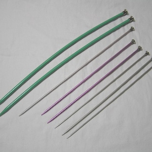 May include: A set of six knitting needles in various sizes. Two green needles, two purple needles, and two silver needles.