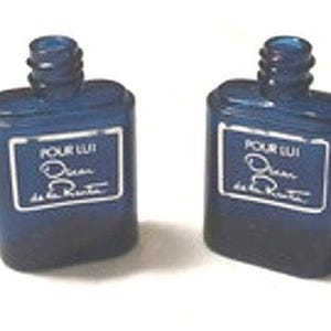 Pode incluir: Dois frascos de perfume azul escuro com uma etiqueta retangular que diz "POUR LUI Oscar de la Renta" em letras brancas. Os frascos têm uma base quadrada e um gargalo cilíndrico.