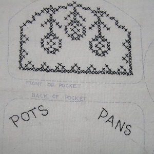 May include: A white fabric with black embroidery of three stylized trees. The fabric is labeled "Front of Pocket" and "Back of Pocket". The words "Pots" and "Pans" are written below the pocket labels.