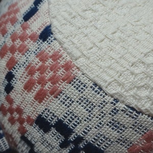 May include: Close-up of a woven fabric with a pink, blue, and white plaid pattern. The fabric has a textured, slightly fuzzy surface.
