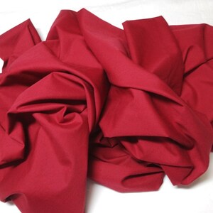 May include: A large piece of solid red fabric, folded and crumpled, with a smooth texture.