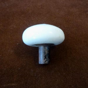 May include: A white mushroom-shaped cabinet knob with a glossy finish. The knob has a rounded top and a dark, textured stem. The hardware is likely for a drawer or cabinet.