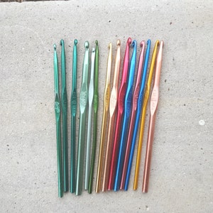 May include: A set of 16 assorted colored crochet hooks. The hooks are made of metal and have a variety of sizes. The hooks are arranged in a row on a light gray surface.