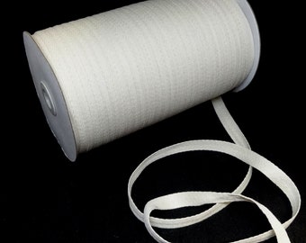 May include: A spool of white cotton twill tape. The tape is rolled up on a cardboard spool and is about 1 inch wide.
