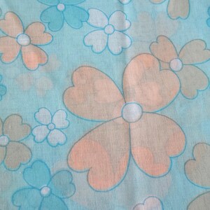 May include: A light blue fabric with a repeating floral pattern. The flowers have peach and light blue petals with white centers. The design is reminiscent of a retro or vintage style.