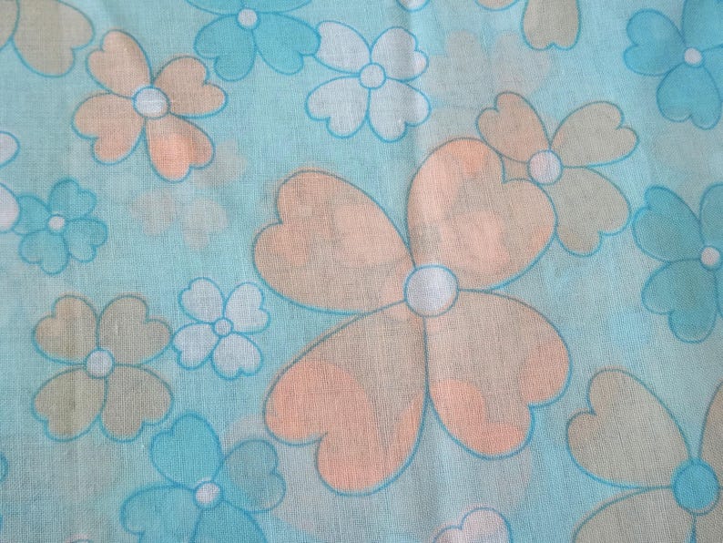 May include: A light blue fabric with a repeating floral pattern. The flowers have peach and light blue petals with white centers. The design is reminiscent of a retro or vintage style.