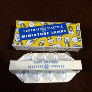 May include: Vintage General Electric miniature lamps in their original packaging. The box is yellow with a blue banner that reads "General Electric Miniature Lamps." The lamps are clear glass with a blue base, and are in a white cardboard holder.