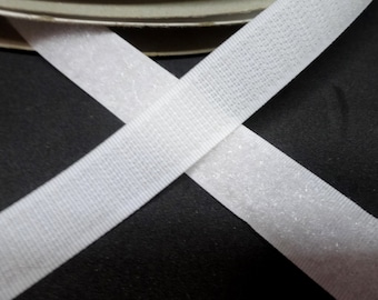 May include: Two white strips of hook and loop fastener tape, also known as Velcro, are crossed over each other on a black background.