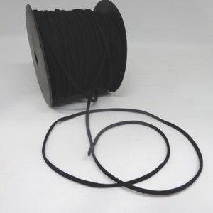 Può includere: Un rotolo di cordoncino in pelle scamosciata nero, con un pezzo di cordoncino svolto e appoggiato su una superficie bianca.