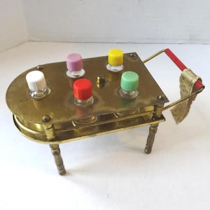 May include: A vintage brass spice rack with six small glass bottles, each topped with a different colored lid: white, pink, red, yellow, and green. The rack has a handle with a red grip and a decorative tag.