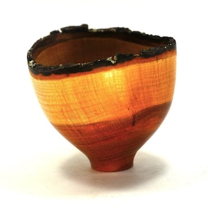 May include: A small wooden bowl with a natural wood finish. The bowl has a dark brown rim and a light brown interior. The bowl is made of wood and has a unique shape.