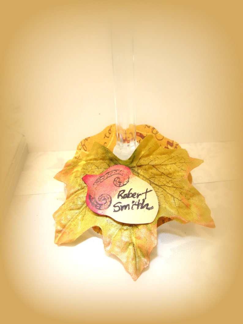 Puede incluir: Una tarjeta de lugar con tem&aacute;tica oto&ntilde;al con un dise&ntilde;o de hoja dorada y una etiqueta de nombre escrita a mano que dice "Robert Smith".