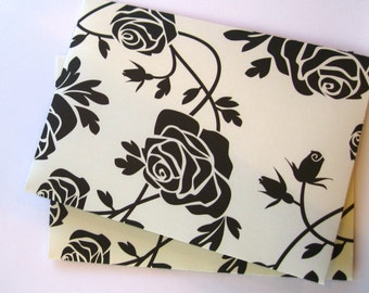 May include: Two sheets of white paper with a black floral pattern. The pattern features black roses and vines.