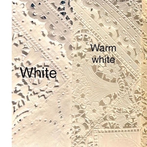 May include: Close-up of white and warm white lace fabric samples. The samples showcase intricate floral and geometric patterns. The text "White" and "Warm white" are visible on the image, highlighting the color variations.