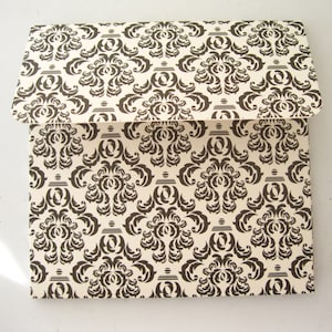 May include: A white envelope with a black damask pattern. The envelope is folded in half and the flap is closed.