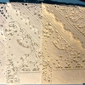 May include: Close-up of several intricately cut paper designs. The designs feature floral and geometric patterns, with delicate cut-out details. The paper has a cream color, and the designs are layered to create depth and texture.