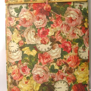 May include: A vintage-style envelope with a floral pattern featuring pink, red, and yellow roses. The envelope has a string closure and a decorative button. The envelope is decorated with several clock faces.