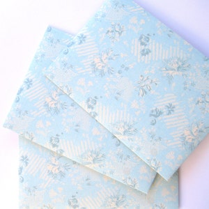 May include: Three light blue envelopes with a white floral pattern. The envelopes are stacked on top of each other.