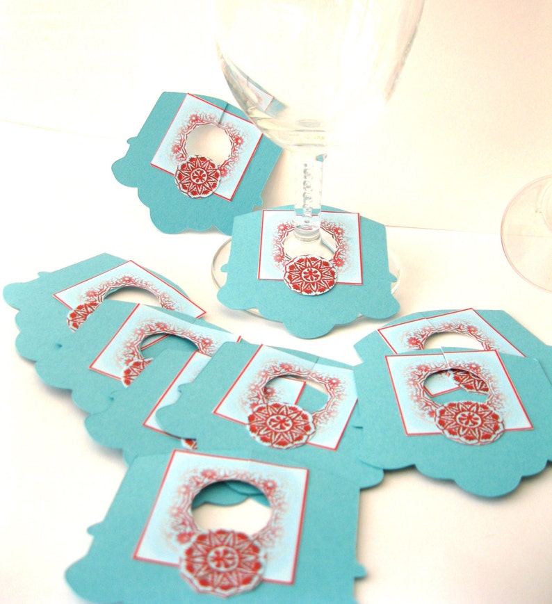 May include: Set of teal blue and red wine glass charms with a decorative design. The charms have a cut-out circle in the center for the stem of the glass.