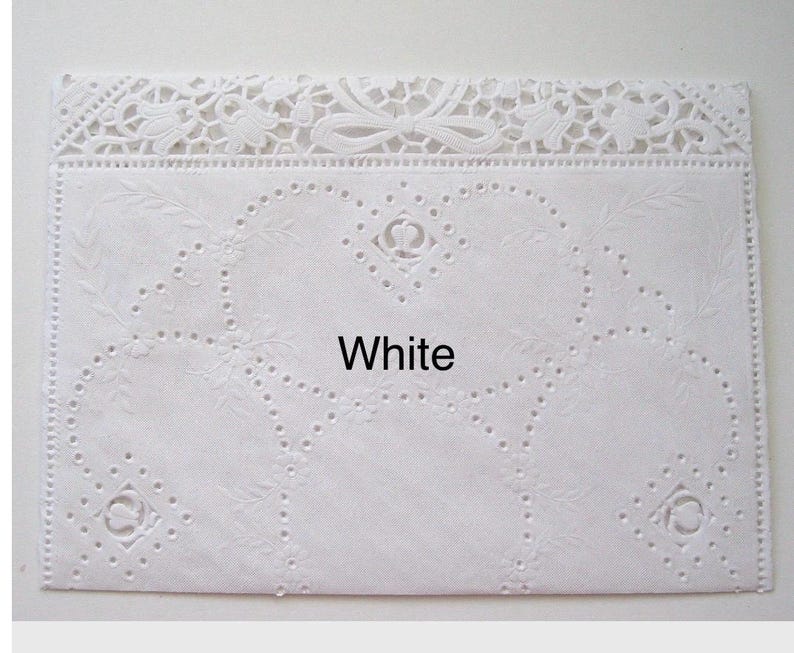 May include: A white, rectangular doily with intricate floral and heart-shaped cutouts. The top edge features a delicate lace design with bows and floral patterns. The word "White" is printed in the center.