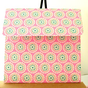May include: A pink envelope with a white and blue patterned design. The pattern features repeating circles with a scalloped edge.