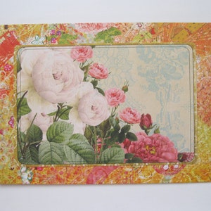 May include: A rectangular greeting card featuring a floral design. The card's central image showcases a bouquet of pink and white roses with green leaves against a light blue and beige background. The card has a decorative, patterned border.