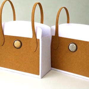 May include: Two white tote bags with tan felt panels on the front and back. Each bag features two tall tan felt handles and a single circular decorative button centered on the tan panel. The left bag has a textured button, while the right has a patterned one.