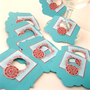 May include: A set of teal blue paper gift tags with red and white snowflake designs. The tags have a hole punched in the top for string or ribbon.