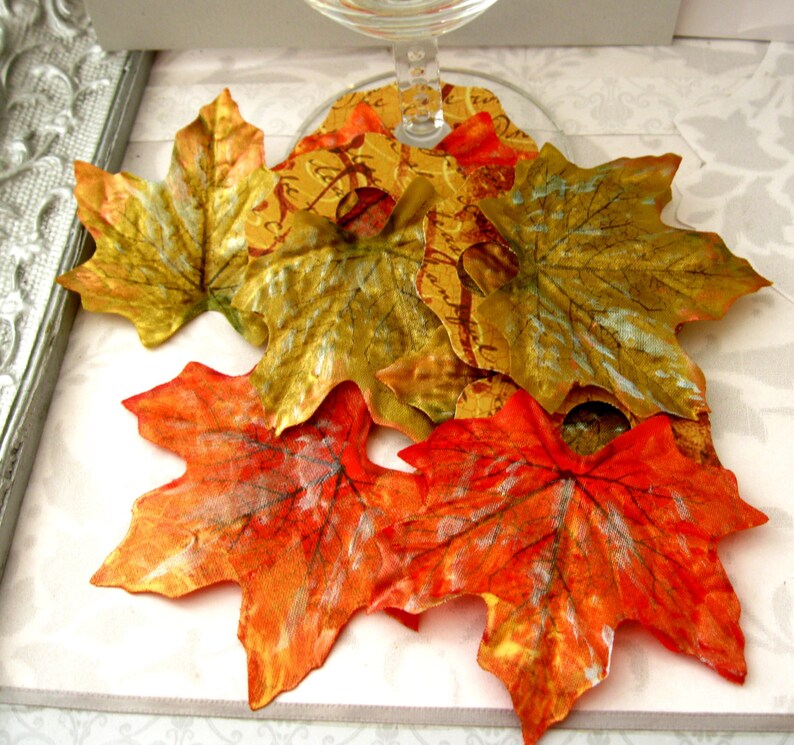 Puede incluir: Una colecci&oacute;n de hojas de arce decorativas de oto&ntilde;o en tonos naranja, rojo, dorado y verde. Las hojas est&aacute;n hechas de un material met&aacute;lico y tienen una superficie texturizada.