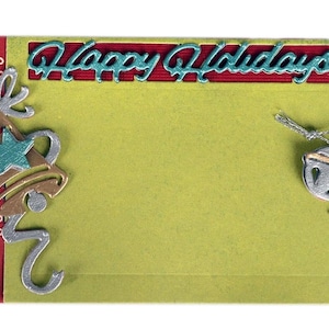 May include: A festive holiday card with a green background and red borders. The words "Happy Holidays" are in teal script. Decorative silver bells, stars, and swirls adorn the card, creating a cheerful seasonal design.