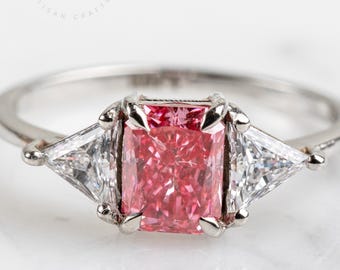 Puede incluir: Primer plano de un anillo de plata con una gema rosa rectangular y dos gemas blancas triangulares. El anillo está sobre un fondo blanco. Se ve el logo de Maison Halo artisan crafted.