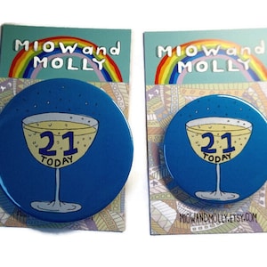 May include: Two blue round 21st birthday buttons with a champagne glass and the text "21 Today" on each. The buttons are on a white background with a rainbow and the text "MIOW and MOLLY" on each.