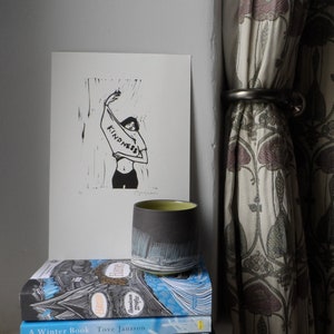 Könnte beinhalten: Ein Stapel von vier Büchern mit blauen und weißen Umschlägen. Das oberste Buch trägt den Titel "Random Family" und den Autor "Adrian Nicole LeBlanc". Das zweite Buch trägt den Titel "A Winter Book" und den Autor "Tove Jansson". Das dritte Buch trägt den Titel "The Salt Path" und den Autor "Raynor Winn". Das unterste Buch trägt den Titel "The Sealwoman's Gift" und den Autor "Anne  Swain". Eine schwarze und grüne Keramiktasse steht auf den Büchern.