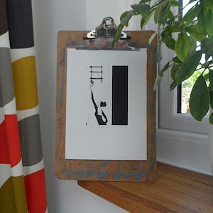 Könnte beinhalten: Ein Schwarz-Weiß-Linolschnitt auf weißem Hintergrund, gerahmt auf einer Klemmbrett. Der Druck zeigt eine Person, die nach einer Leiter greift. Der Text "By Jess Wilson" und "Linocut" ist unter dem Bild gedruckt.