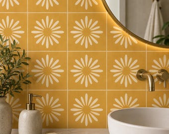 May include: Square wall tiles in a vibrant mustard yellow featuring a repeating white daisy-like floral pattern. The tiles are arranged in a grid formation, creating a continuous graphic design across the wall surface behind a bathroom sink.