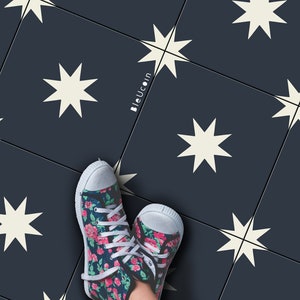 Op de afbeelding: Een paar high-top sneakers met bloemenprint, witte veters en neus. De sneakers hebben een donkerblauwe achtergrond met een patroon van roze en rode rozen. De persoon draagt een blauwe spijkerbroek. De achtergrond is een donkerblauwe tegel met witte sterpatronen.