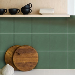 May include: A kitchen backsplash with green square tiles. There are two wooden cutting boards and a white ceramic vase on the counter below the backsplash.
