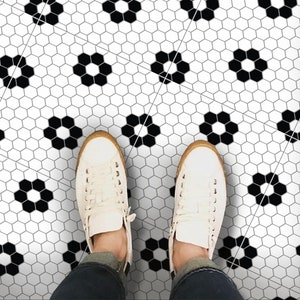 Puede incluir: Azulejos hexagonales blanco y negro con un patrón de flores. Un par de zapatillas blancas están de pie en el suelo.