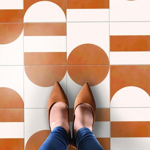 May include: A pair of brown shoes with pointed toes stand on a floor with a geometric pattern of white and orange tiles.